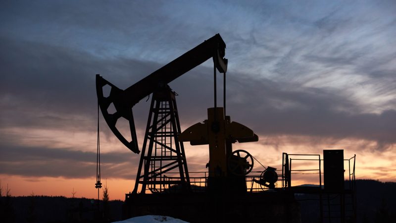 View of evening dramatic sky over long stroke balanced beam petroleum pump jack. Oil field with oil pumping unit or oil pump rocker-machine during sunset. Concept of petroleum industry, oil extraction